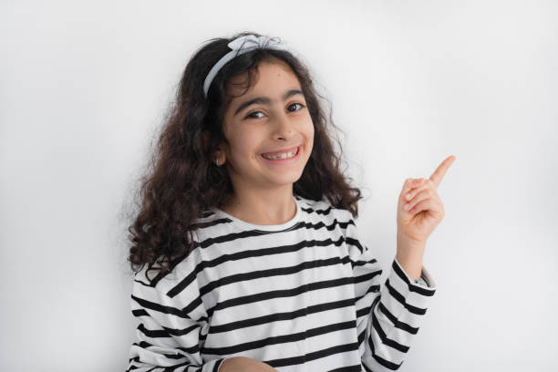 Happy little girl pointing fingers at copy space isolated over white background