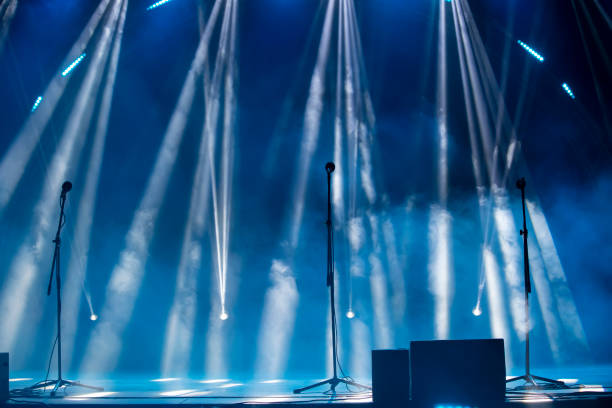 istock Blurred rays of light from stage spotlights on a blue stage background with microphones. The beginning of a concert or show. 2040186685