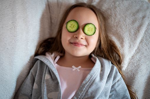 Little girl with a cucumber eye mask in her living room
