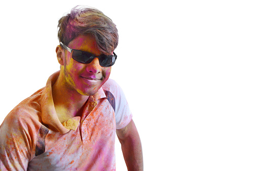 Cut out of Horizontal waist up portrait of one stylish cool happy smiling young 16 year old Indian Asian boy in black sunglasses goggles with smile on face, looking at camera painted messy with Holi festival powder colours isolated over white background.