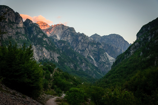 Panorama of peaks of the Montenegrin mountain massif Durmitor with slopes covered with mountainous green vegetation and pedestrian winding tourist paths against the background of evening cloudy sky