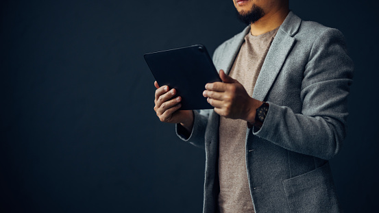 A cropped view of a business professional interacting with a digital tablet, set against a dark backdrop, symbolizing connectivity.