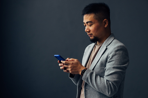 Focused businessman in a grey suit using a smartphone. Conceptual image for connectivity, technology, and corporate lifestyle.