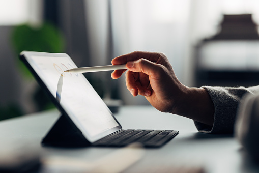 Close-up of a hand using a stylus on a digital tablet, focused work environment, technology in business.