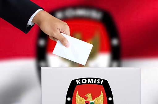 The man’s hand in a casual black suit is inserting a ballot into an election ballot box.pemilu Indonesia concept.