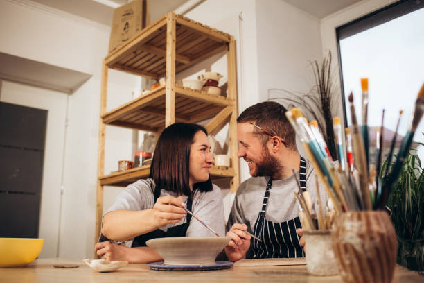Couple in love working together on potter wheel in craft studio workshop.