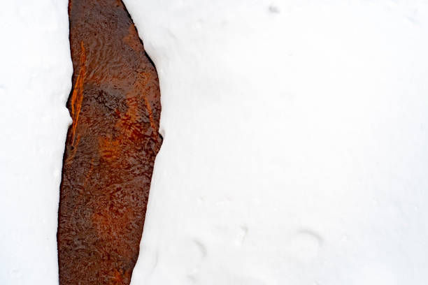 Background with a frozen river surrounded by snow with empty space for text. A natural stream of red color in an iron-rich area.