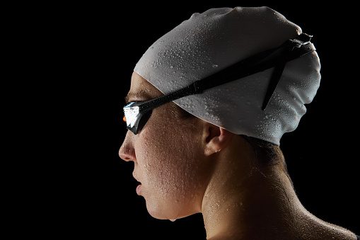 Close up. rear view portrait of young athletic woman with waterdrops on face after swimming race against black studio background. Concept of professional sport, motion, strength and power. Ad