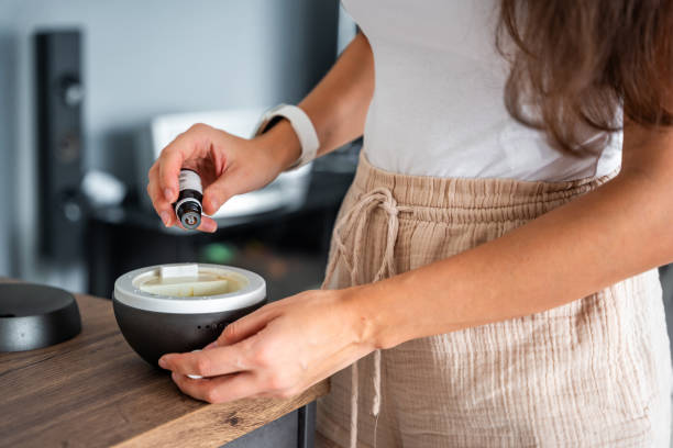 Woman adding oil to the grey aroma oil diffuser on light table at home, air freshener Woman adding oil to the grey aroma oil diffuser on light table at home, air freshener. High quality photo home diffuser stock pictures, royalty-free photos & images