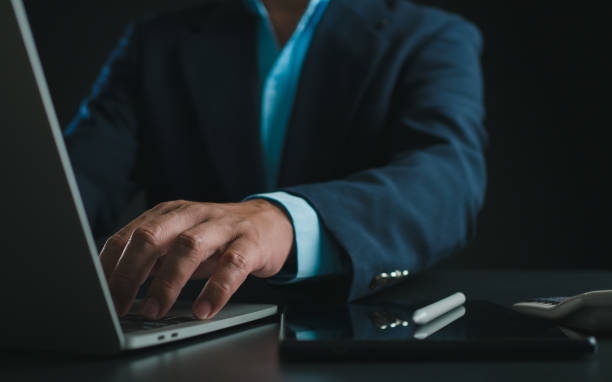 istock Businessman in black suit working on laptop computer and tablet, Hand typing on keyboard on table at office with dark background, Online working, Close up, Copy space. 2040285800