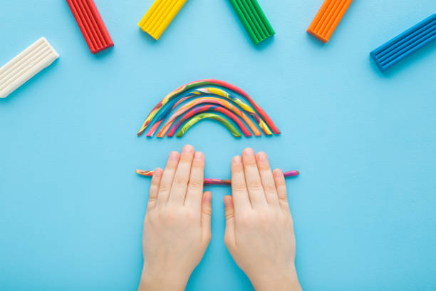 istock Baby boy hands rolling colorful stick from modeling clay on light blue table background. Pastel color. Closeup. Point of view shot. Toddler development. Making multicolor rainbow shape. Top down view. 2040303015