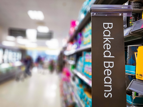 Close up of a sign with the words 'baked beans' in a supermarket aisle.
