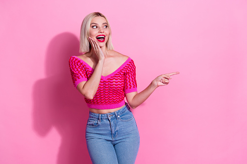 Photo of overjoyed pretty woman dressed knitwear clothes look directing at sale empty space arm on cheek isolated on pink background.