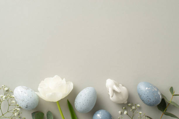 istock Spring celebration theme in top view photo featuring slate greyish eggs, a bunny statuette, gypsophila, tulip, and eucalyptus arrayed on a soft grey canvas, with a void for text or advertising 2040341526
