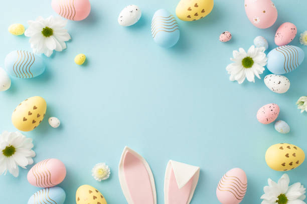 istock Easter art concept: top view of vivid eggs, charming rabbit ears, and chrysanthemum buds on a gentle blue surface, leaving space for text or advertising 2040342635