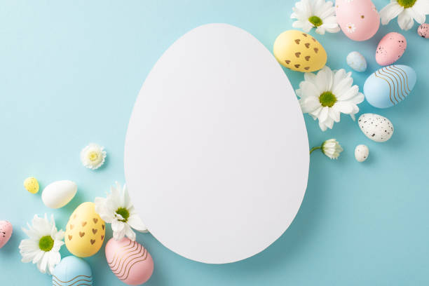 istock Easter design concept: Flat lay top view of dyed eggs, and chamomile buds on a pastel blue surface with open egg-shaped frame for text or advertising 2040342639