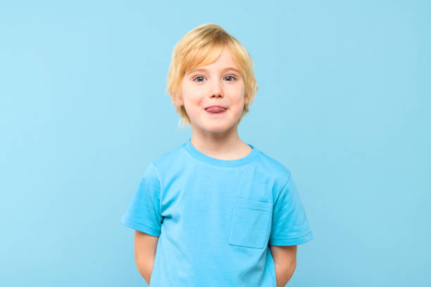 funny young boy showing tongue and looking at the camera over pastel blue background. cute preschooler grimacing at camera sticking out his tongue. - preschooler caucasian one person part of ストックフォトと画像