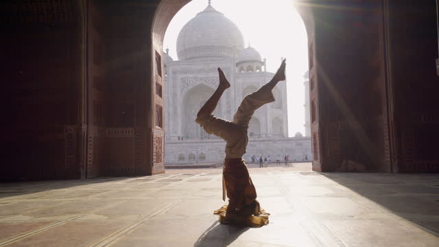 Young woman practicing yoga in India at the famous Taj Mahal at sunrise - Headstand position upside down- People travel spirituality zen like concept