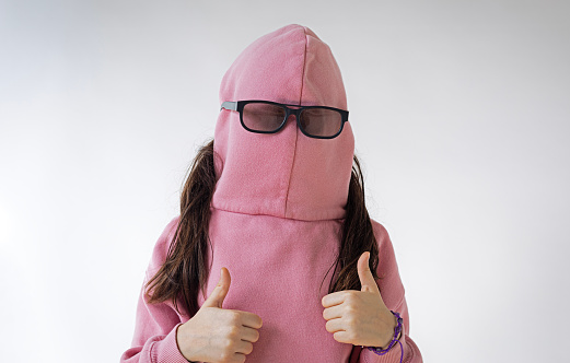 The girl, wearing a sweatshirt against a white backdrop, hilariously obscures her face with her backwards cap while donning sunglasses.