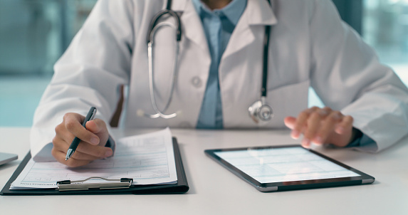 Person, doctor and hands with tablet, clipboard or documents in research or planning at hospital. Closeup of medical or healthcare professional filling paperwork, life insurance or form at clinic