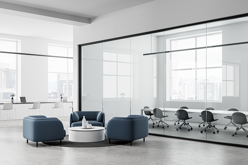 Corner view of white office interior with relax place, armchairs and coffee table on concrete floor. Coworking zone with laptop and glass meeting room. Panoramic window on Kuala Lumpur. 3D rendering
