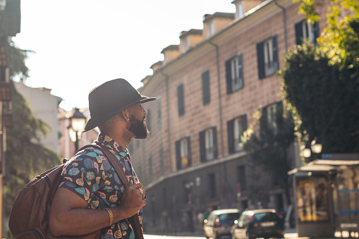 Stylish black man with alternative hipster look walking through the streets of a city on a sunny summer day. he smiles happily