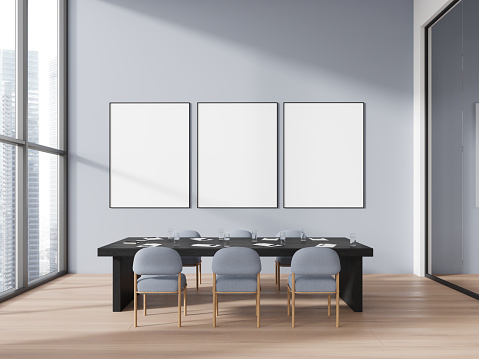 Cozy conference interior with blue chairs and black table, hardwood floor. Glass meeting room with stylish furniture, mockup canvas posters in row. 3D rendering
