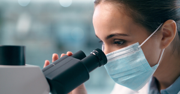 Woman, scientist and face mask with microscope in forensic, research or discovery at laboratory. Closeup of female person, medical or healthcare professional looking in scope, scientific data or lab