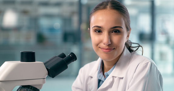Face, scientist and happy woman on microscope in laboratory in research. Portrait, science and medical professional doctor on equipment for experiment of expert, worker and healthcare employee smile