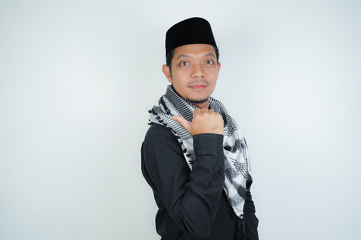 Cheerful handsome Asian Muslim man wearing Arab turban sorban pointing hand finger at empty space for advertising on isolated background