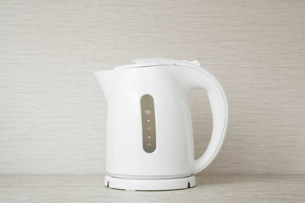 New white plastic electric kettle on stone table top at wall background. Closeup. Front view.