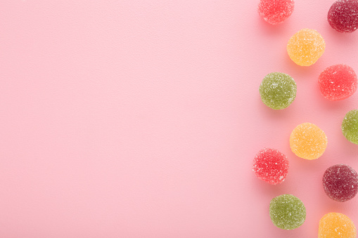 Sweet colorful candied fruit jelly with sugar grains on light pink table background. Pastel color. Closeup. Empty place for text. Top down view.
