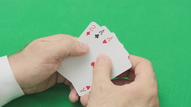 man hand opens poker combination of two pairs - aces and deuces, on background of green cloth, close-up, slow motion