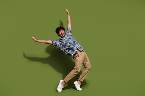Full body length photo of indian positive guy standing tiptoes raised hands up having fun in nightclub isolated on khaki color background.