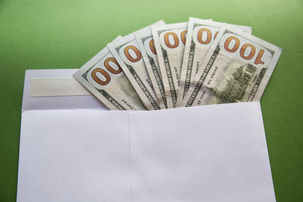 Hundred-dollar bills peeking out of a white envelope on a green background