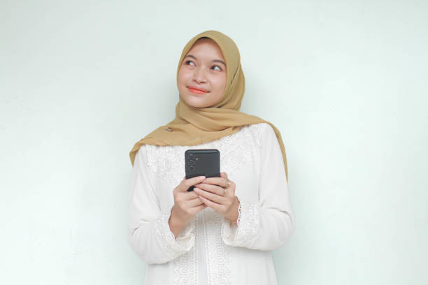 istock Young Asian Muslim woman holding mobile phone with thinking something. 2040419974