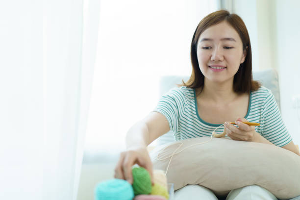 horizontal low angle portrait of senior woman sewing with wool on the sofa at home happy doing craft activity
