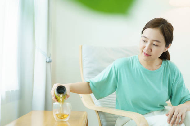 Delightful Asian middle adult woman relaxing and sitting on the cozy lounge chair and drinking a cup of tea in the morning. Beautiful - good looking Asian young woman enjoying a cup of hot tea in morning.