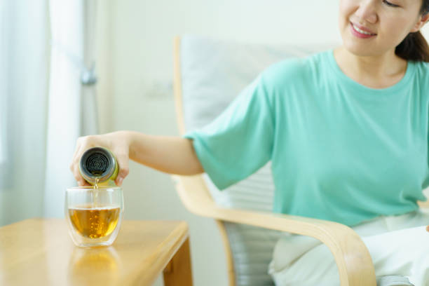 Delightful Asian middle adult woman relaxing and sitting on the cozy lounge chair and drinking a cup of tea in the morning. Beautiful - good looking Asian young woman enjoying a cup of hot tea in morning.