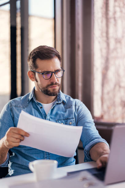 istock Satisfied young man with glasses sitting at a desk and doing paperwork at his workplace. 2040446312