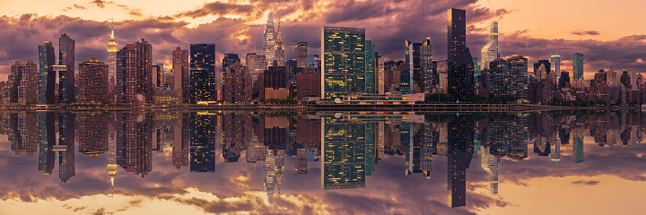 High Resolution Stitched Panorama of New York Skyline with UN Building (Headquarters of the United Nations), Chrysler Building, Empire State Building, Manhattan Upper East Side Residential and Office High-rises, FDR drive, Green Trees and Dramatic Sunset Sky with Clouds all reflected in  water of East River. Canon EOS 6D (Full Frame censor) DSLR and Canon EF 85mm f/1.8 lens. 3:1 Image Aspect Ratio. This image is downsized to 50MP. The Original image resolution is 119MP or 18,923 x 6,308 px.