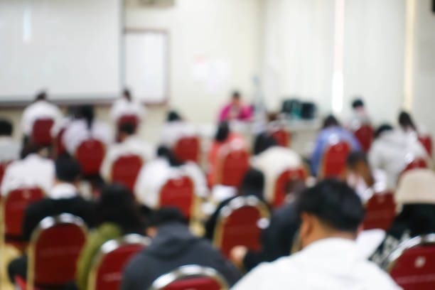 Blurred abstract background of examination room with undergraduate students inside. Blurred view of a student doing the final test in the exam room. Blurry view of study chairs in university.