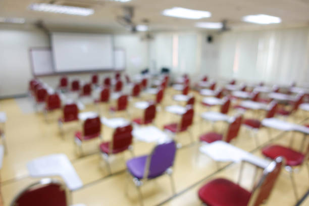 Blurred abstract background of examination room with undergraduate students inside. Blurred view of a student doing the final test in the exam room. Blurry view of study chairs in university.