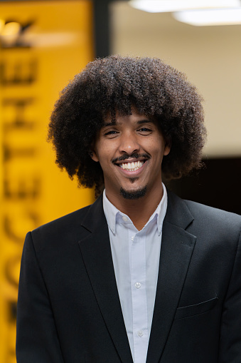Friendly businessman with afro hair wearing a suit, smiling confidently in a corporate setting.