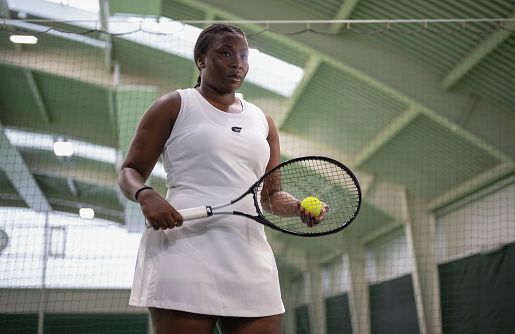 Portrait of young female tennis player standing in indoor tennis court. Sport and healthy lifestyle concept.