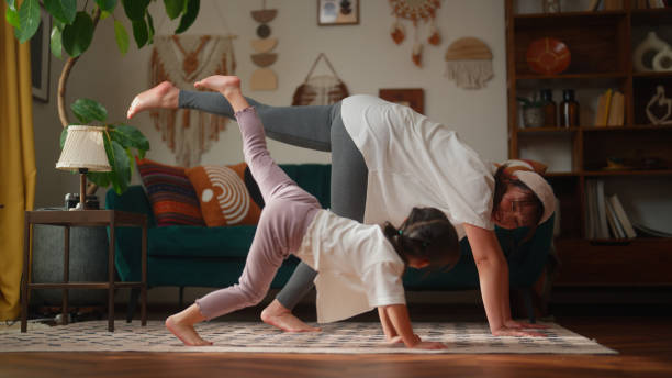 Mother and her small daughter practicing yoga in the living room at home A mother and her small daughter are bonding and practicing yoga in the living room at home. japan small apartment stock pictures, royalty-free photos & images