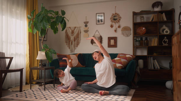 Mother and her small daughter practicing yoga in the living room at home A mother and her small daughter are bonding and practicing yoga in the living room at home. japan small apartment stock pictures, royalty-free photos & images