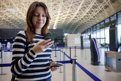 Smiling young woman with backpack checking her boarding schedule at the airport
