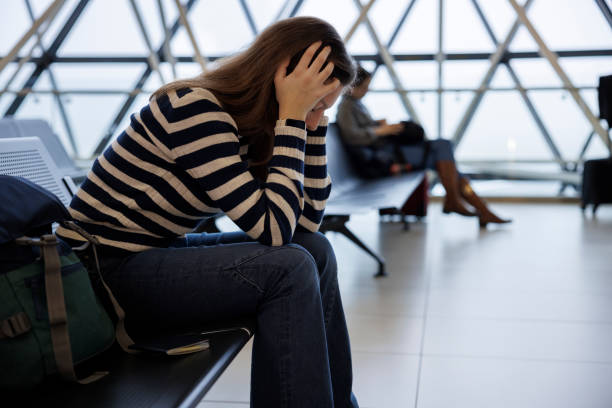 공항에 앉아서 지연된 출발, 탑승 또는 출입국 심사를 기다리는 좌절한 젊은 여성 스톡 사진