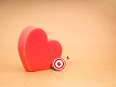 Love match, couple finding mission, matching partners online concept. Small red 3d target icon ig red bold sponge heart shaped, isolated on recycle kraft paper background with copy space.